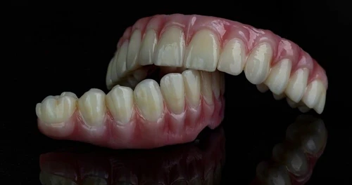Upper and lower full dental dentures with pink gums on black reflective surface.